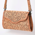 Brown leather handbag with intricate floral patterns on a white background