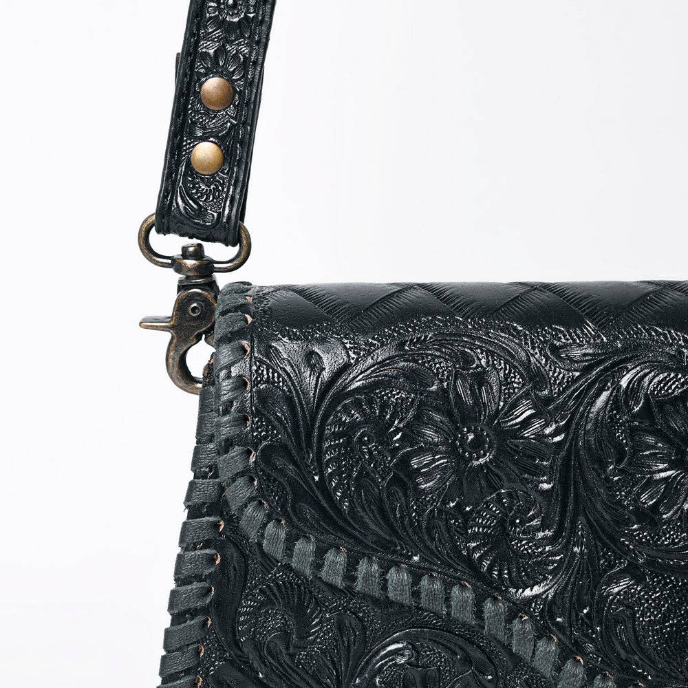 Black leather handbag with intricate floral tooling and gold accents on a white background